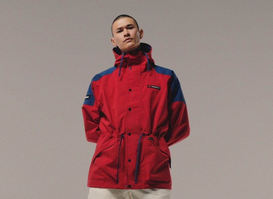 A man is standing and wearing a red and blue jacket.